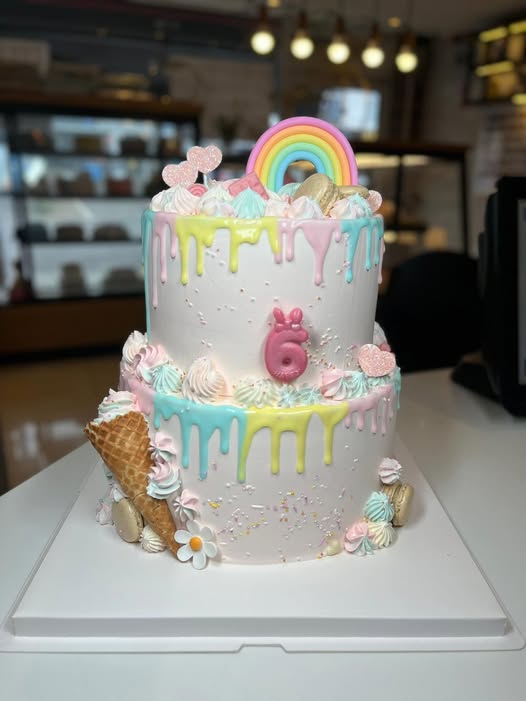 Pastel two-tier drip cake with a rainbow topper, macarons and ice cream cones