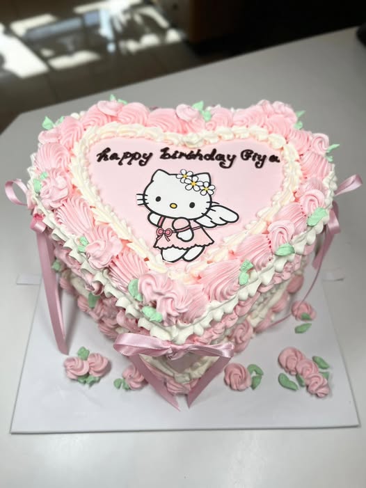 Pink heart-shaped vintage birthday cake with piped rosettes, ribbons and a character plaque