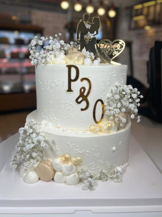 Two-tier ivory wedding cake with gypsophila, pearls and gold monogram, made in Grays, Essex