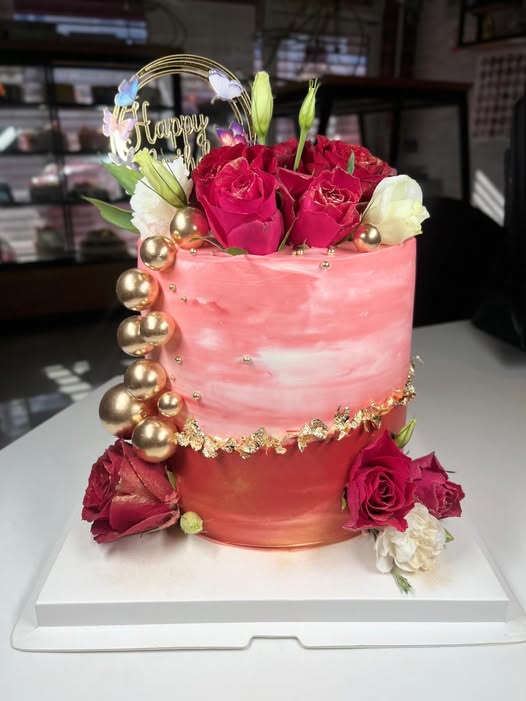Coral and gold marbled birthday cake with fresh roses, gold spheres and gold leaf