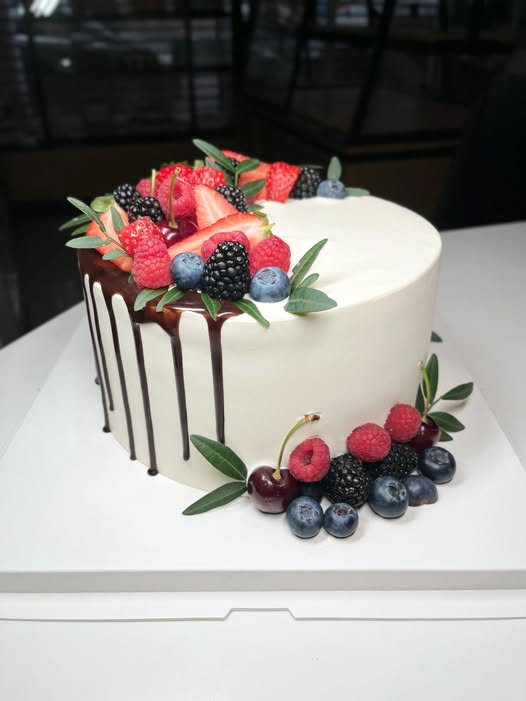 Smooth ivory cake with dark chocolate drip and fresh berries, made in Essex