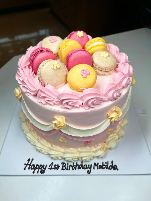 Pastel first birthday cake with piped ruffles and a crown of pink and yellow macarons