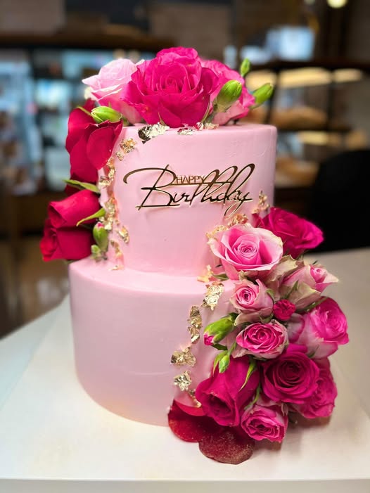Two-tier pink buttercream birthday cake with cascading fresh roses and gold leaf