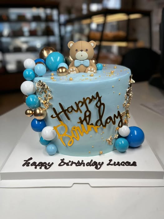Blue buttercream birthday cake with a teddy bear topper, gold leaf and balloon spheres
