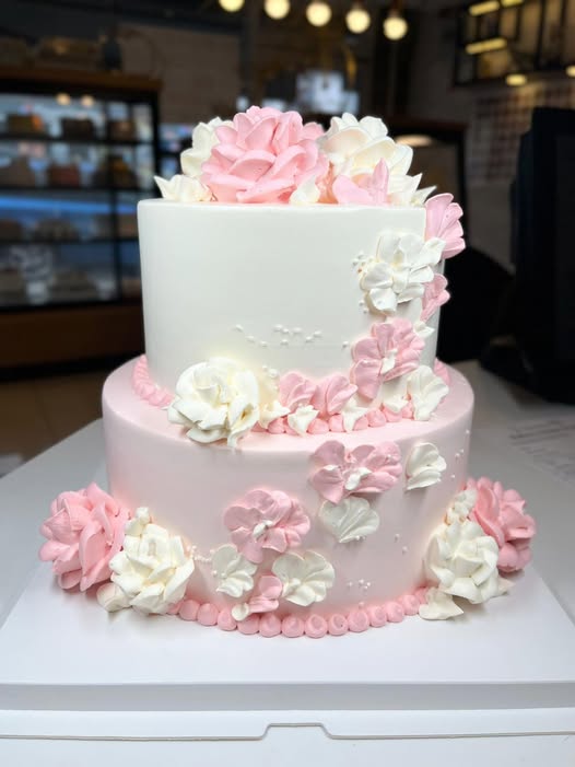 Two-tier pink and ivory celebration cake covered in hand-piped buttercream blossoms