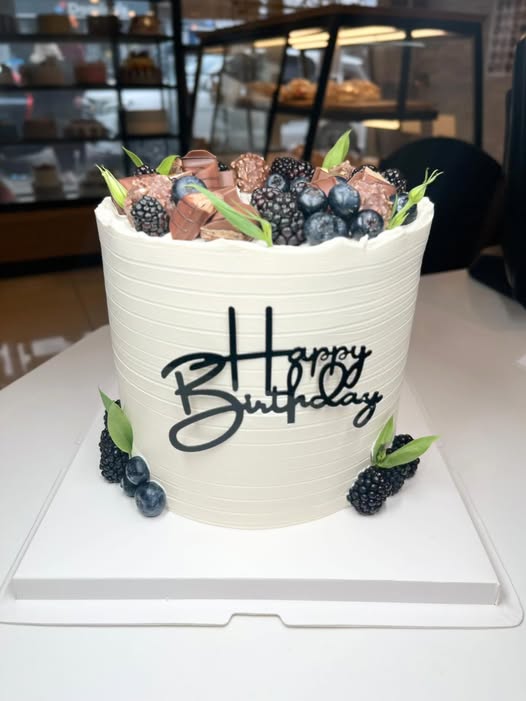 Tall ivory birthday cake topped with chocolate, blackberries and blueberries